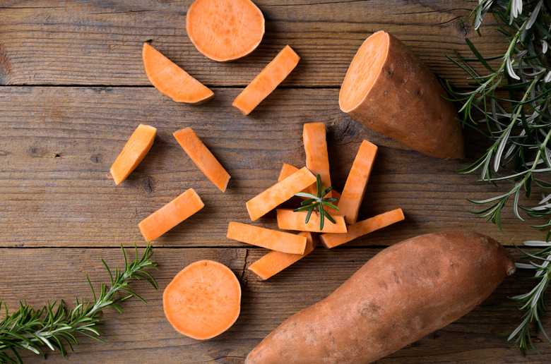 Raw whole orange sweet potato and slices of batatas with fresh rosemary on rustic wooden background