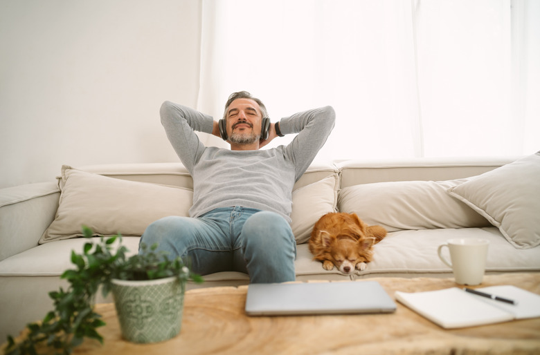 Calm Middle age Caucasian man sitting on sofa listening to music enjoying meditation for sleep and peaceful mind in wireless headphones