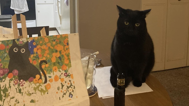 black cat standing next to painting of black cat.