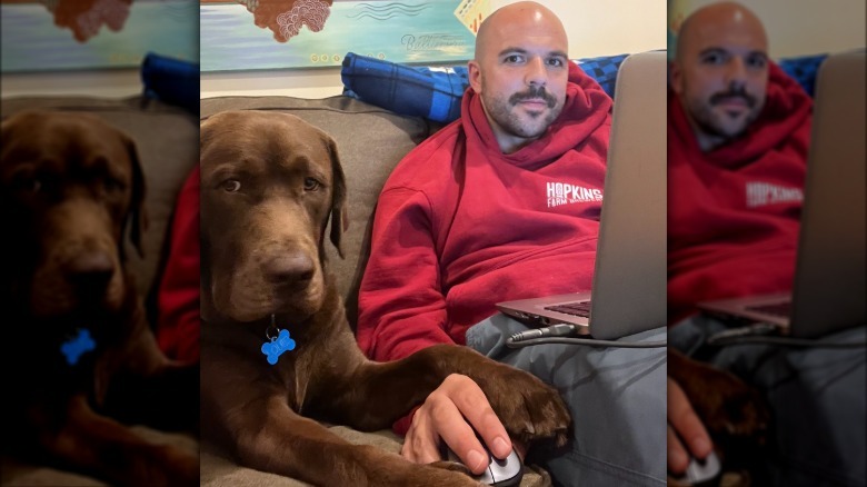 dog holds mans hand on computer mouse.