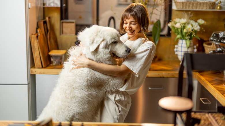 A smiling woman hugging a Great Pyrenees that's standing on its toes.