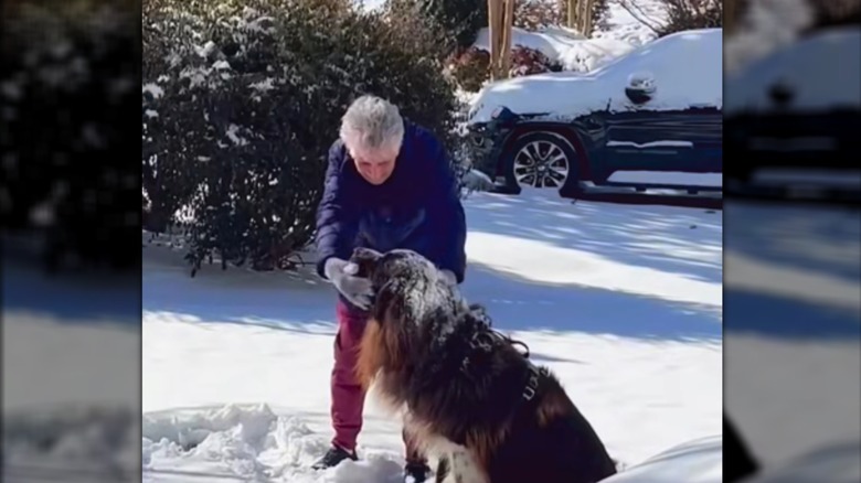 A woman in parka leaning over to pet a snow-covered dog.