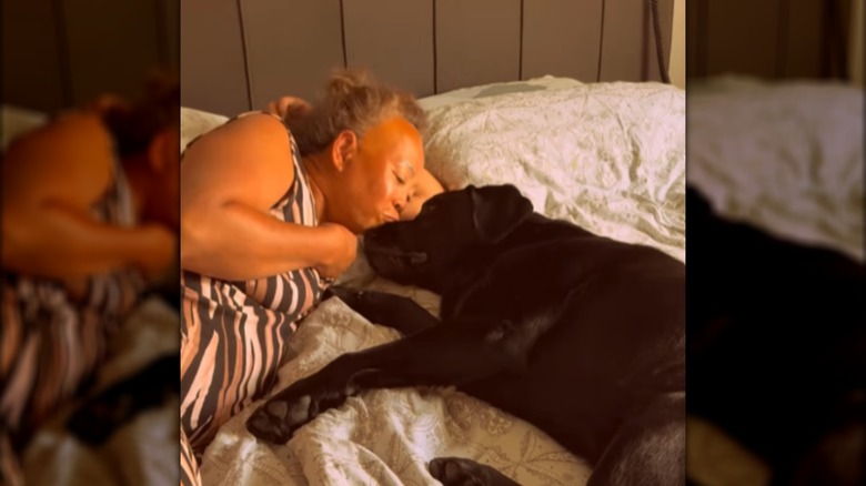 A woman lying in bed, kissing a black dog.