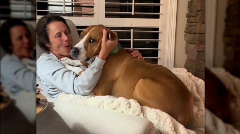 A woman cuddling a large brown dog on a chair.
