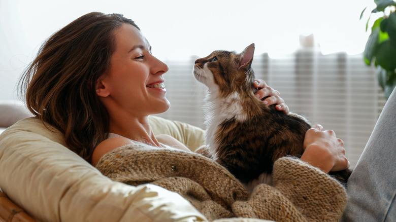 A woman holding her pet cat while sitting on the sofa