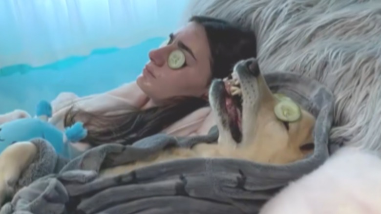 A woman and a dog lying on their backs with cucumbers over their eyes.