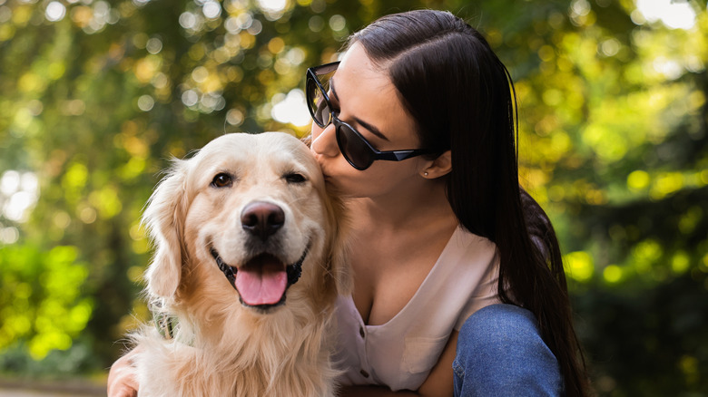 Woman wearing sunglasses kisses head of happy dog