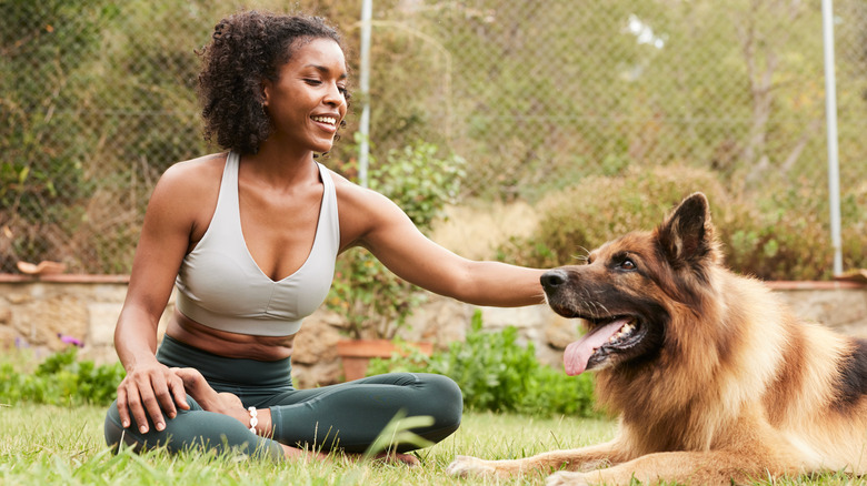 A young woman reaches out to pet her long-haired German shepherd dog