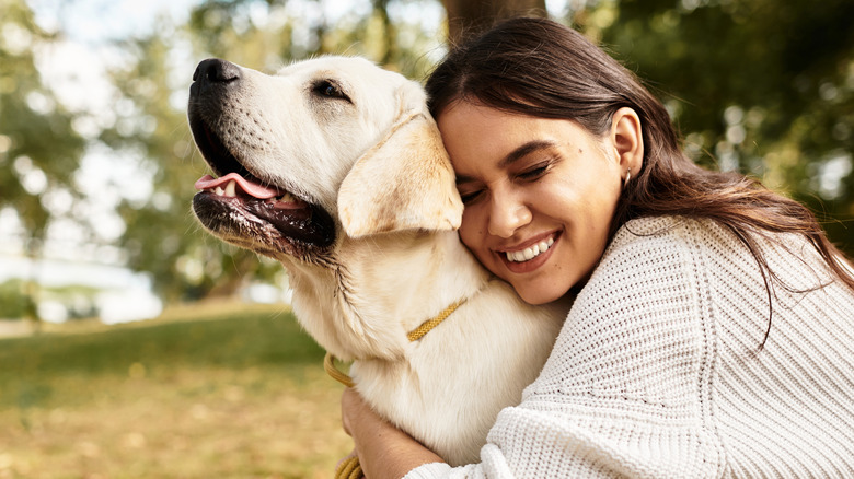 A young woman leans her head against a Labrador retriever