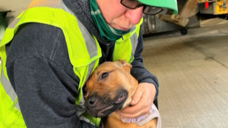 A man in glasses and a yellow safety vest hugging a dog.
