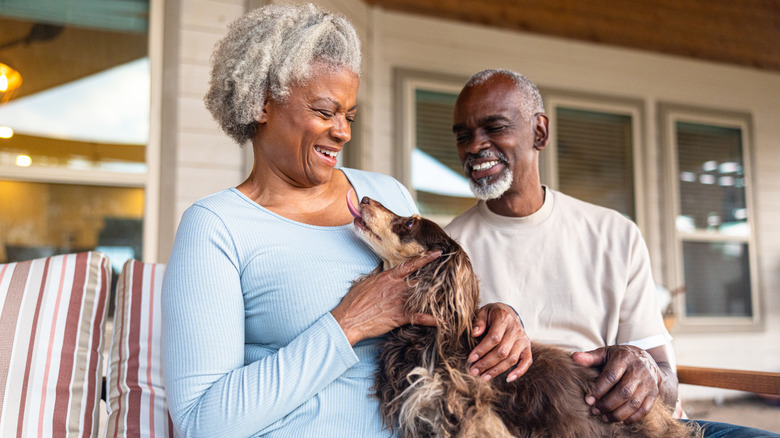 Senior Black couple at home cuddling with their longhaired dachshund dog.