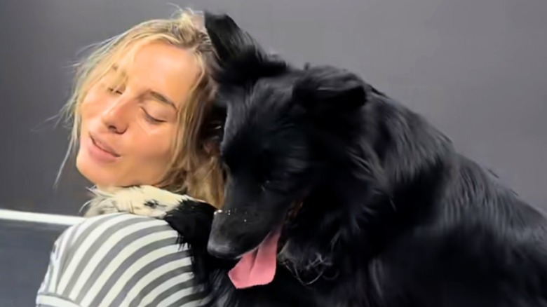 Black border collie places paws on woman with blonde hair's shoulder.