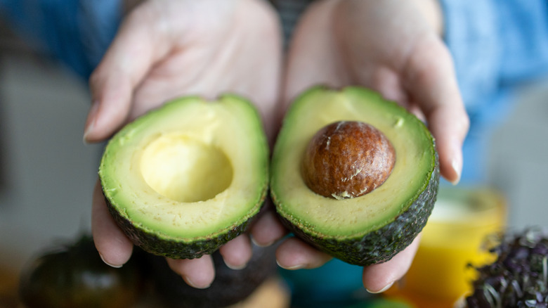 Hands holding a halved avocado