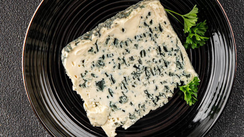 A fancy, moldy cheese on a black plate with sprigs of parsley