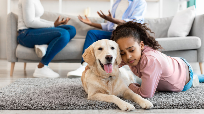 A sad girl cuddles her dog while her parents argue in the background