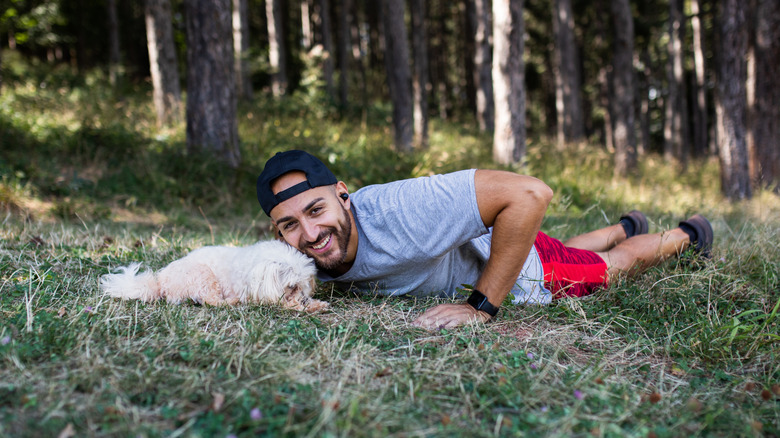 Man doing pushups in woods with small dog nearby