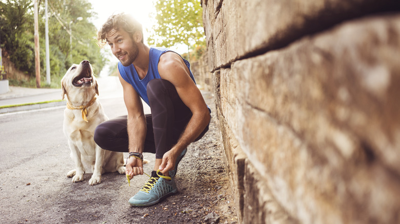 Man lacing up his running shoes outside with his dog nearby
