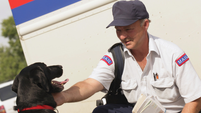 A mail carrier petting a black dog