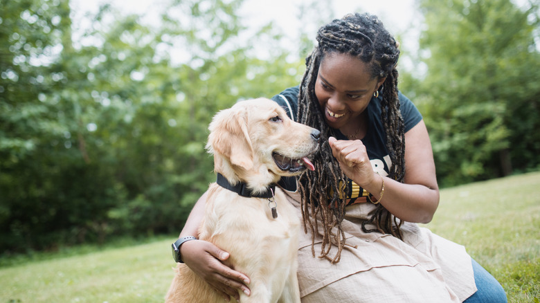 A long-haired woman playing with a golden retriever outside.