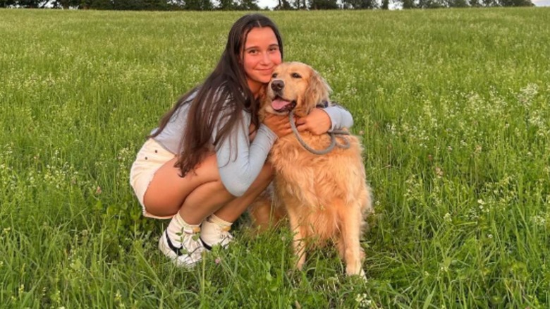 A golden retriever owner posing with her dog in a grassy area