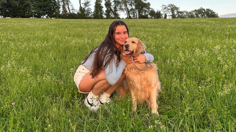 A golden retriever owner posing with her dog in a grassy area