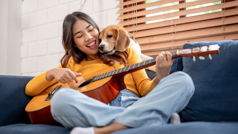 Asian woman sitting on sofa with guitar with a beagle snuggling up behind her
