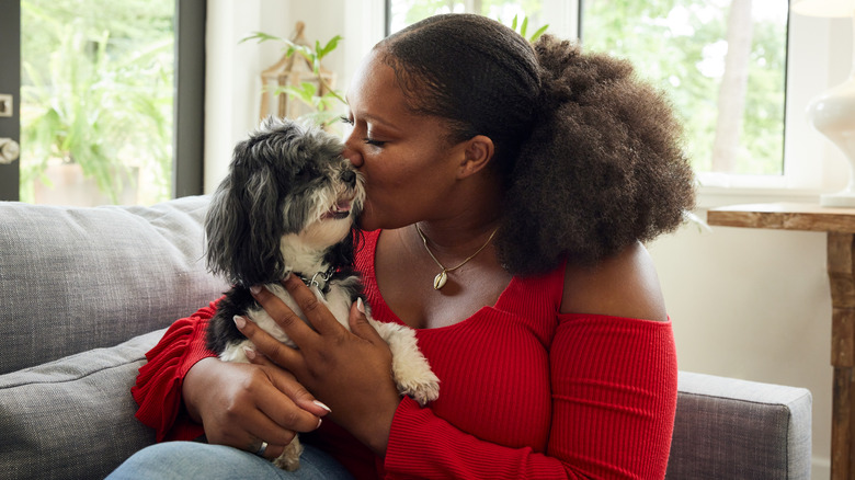 Black woman kissing her dog on sofa