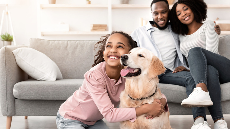 A young girl hugs a happy golden retriever as her smiling parents look on