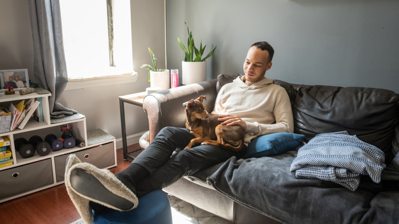 Man with his feet up in a small NYC apartment, dog on his lap