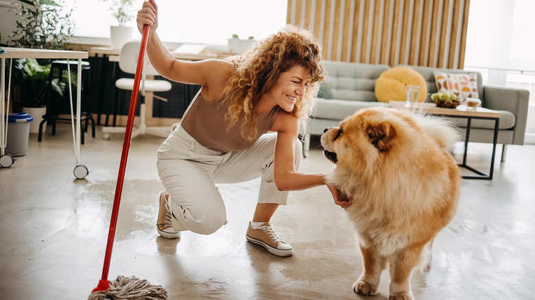Woman holding a mop and petting a dog.