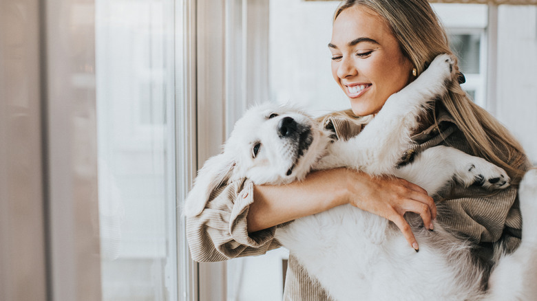 A smiling woman holding a golden retriever puppy.