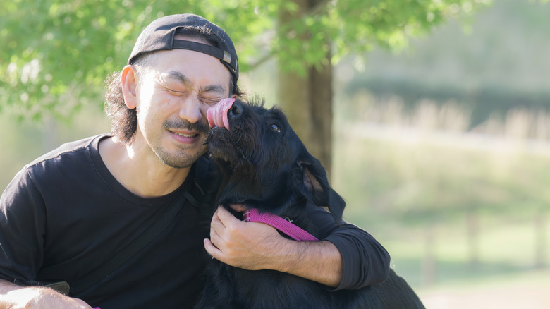 A man gets kisses from his dog while cuddling outside.
