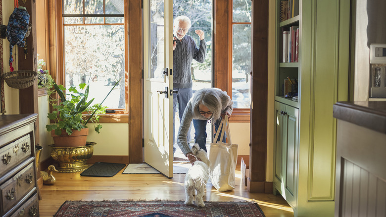 An older couple greets a white dog at the door.