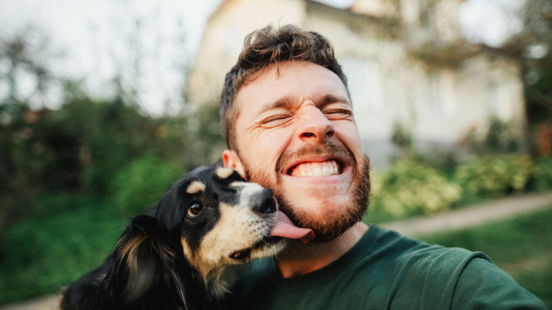 A dog licking a smiling man's beard outdoors.