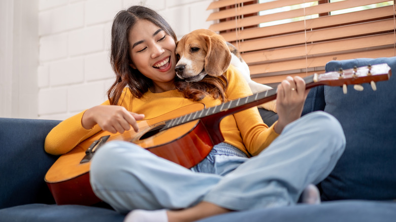 A dog loving on its human while she plays guitar