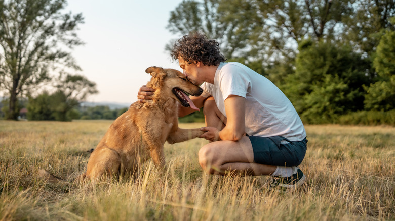Man outdoors kneeling to kiss his dog on snout