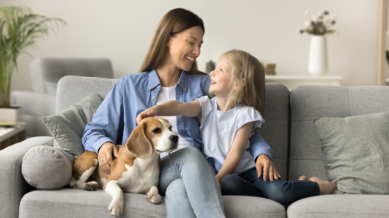A mother and child sit on couch petting dog.