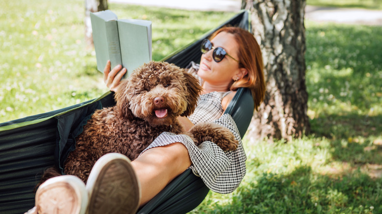 Happy woman reading a book and happy dog lying in a hammock