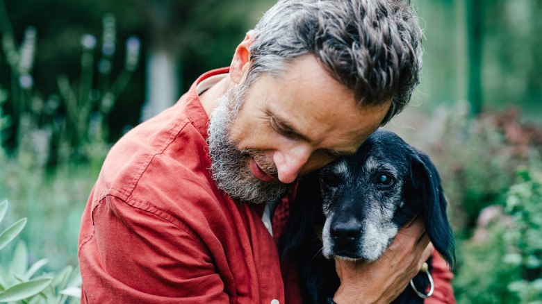 Man hugging senior dog with affection.