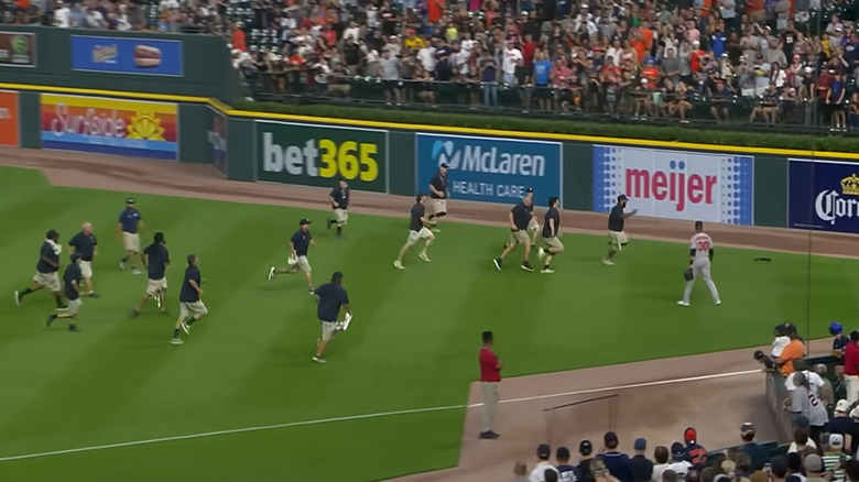 Squirrel being chased by more than a dozen people on a baseball field