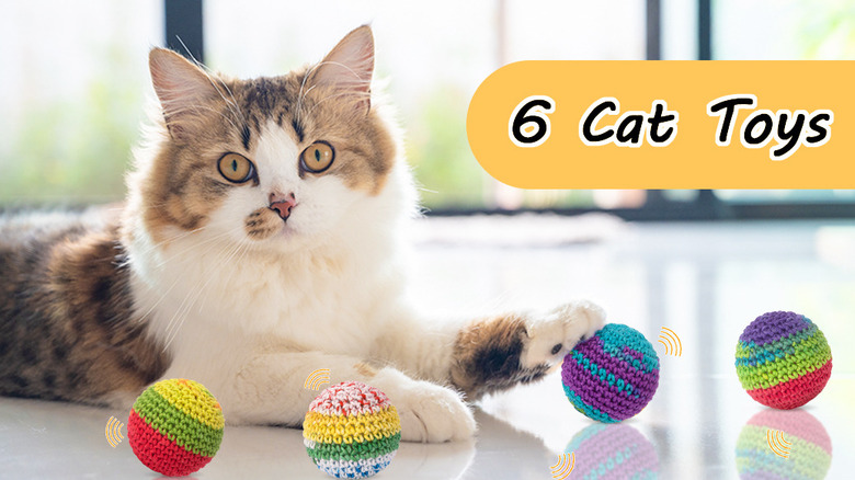 A yellow-eyed cat lying next to colorful yarn balls