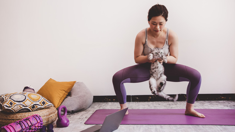 Woman doing squats while holding her cat
