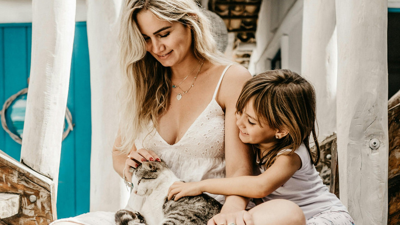 Woman sitting with a kid, petting a cat.