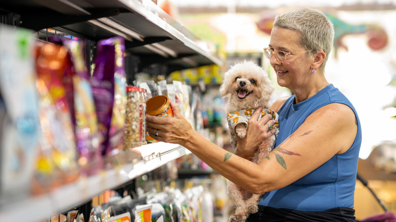 Woman holding happy poodle dog while looking at food in pet store