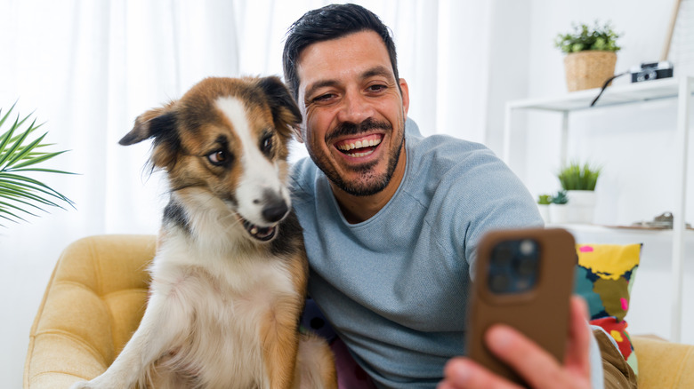 Man taking photo with dog on couch.