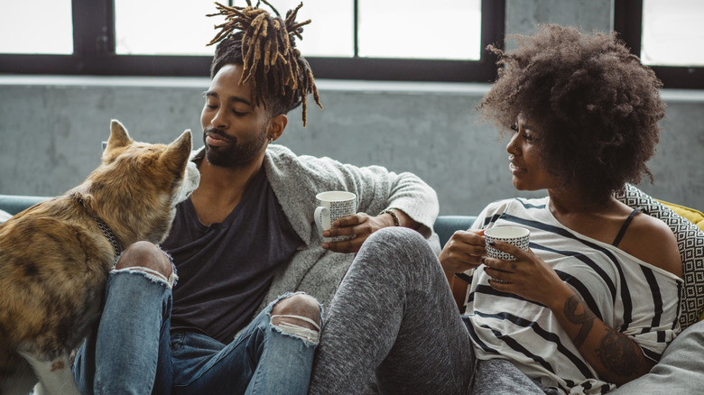 Man and woman sitting on sofa, man starting at dog sitting beside him