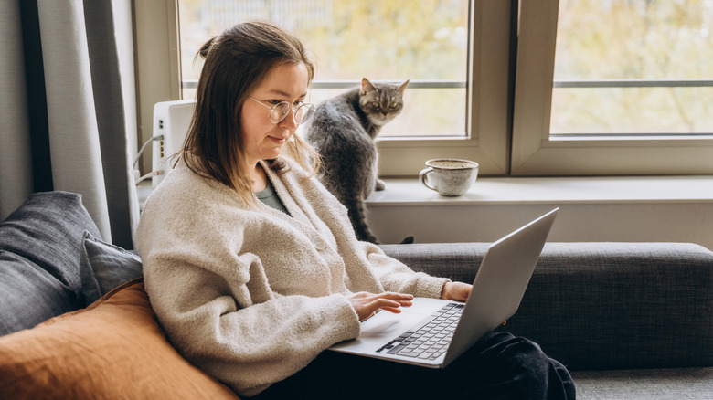 Woman seated in living room with laptop, cat in background