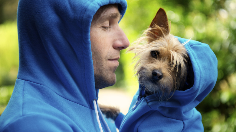 Man in sweatshirt holds a dog that's in a matching sweatshirt.