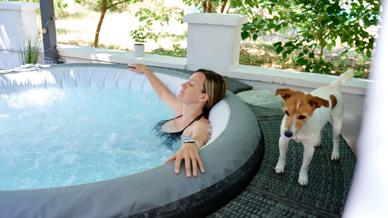 A woman in a hot tub with a dog waiting outside.