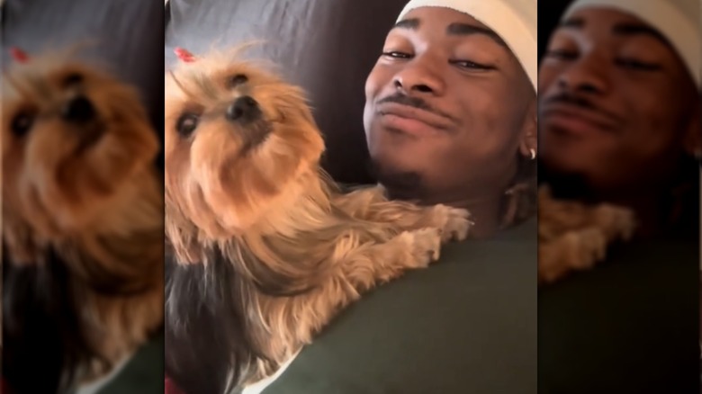 Yorkie howls in bed beside a Black person wearing a white durag.